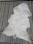 A soft natural white and light brown british isles sheepskin rug with fluffy texture on a wooden deck