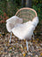A cozy off-white british isles sheepskin rug draped over a woven rattan chair with white metal legs