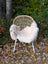 A cozy cream british isles sheepskin throw draped over a woven wicker chair with white metal legs