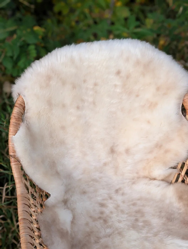 A soft fluffy off-white british isles sheepskin rug with natural texture resting in a woven wicker basket