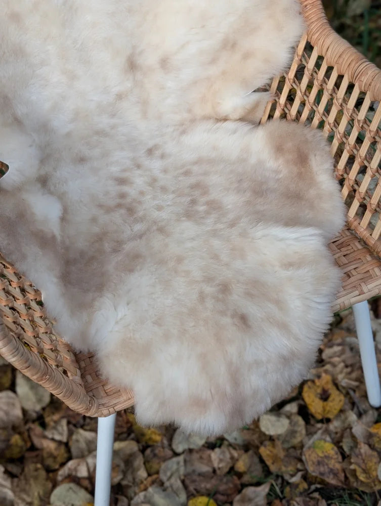 A soft cream-colored british isles sheepskin rug with fluffy texture and subtle brown speckles measuring 46 x 24 inches