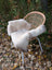 A soft creamy white british isles sheepskin throw draped over a woven wicker chair with metal legs
