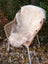 Cream-colored british isles sheepskin rug draped over woven wicker chair with white metal legs for cozy decor