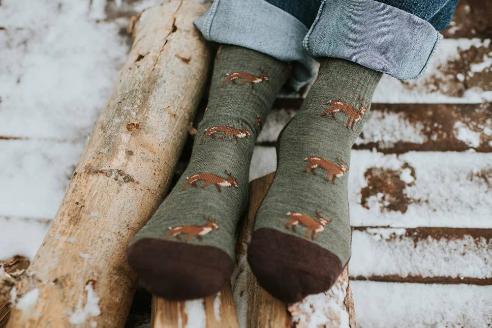 Men’s olive green merino wool socks with brown deer prints and dark brown toe caps worn with rolled-up jeans