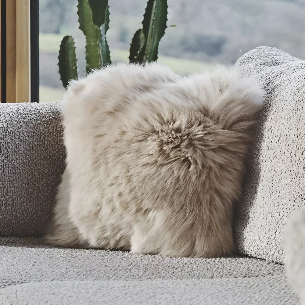 Fluffy beige faux fur sheepskin cushion with cotton back resting on textured gray couch for cozy decor