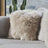 Fluffy beige faux fur sheepskin cushion with cotton back resting on textured gray couch for cozy decor