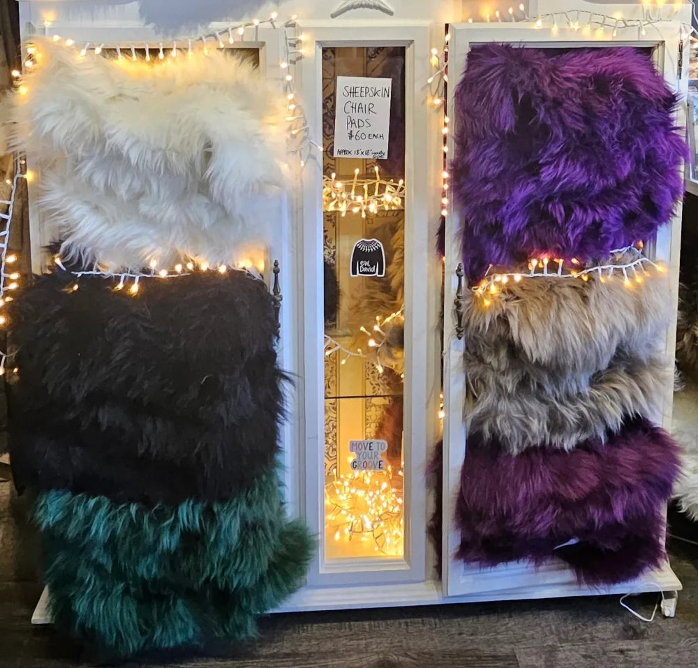 Plush merino sheepskins dyed colors in white black teal purple and beige displayed as chair pads on shelves