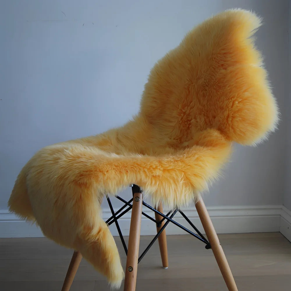 A plush golden-yellow dyed merino sheepskin draped over a modern wooden-legged chair with black metal frame