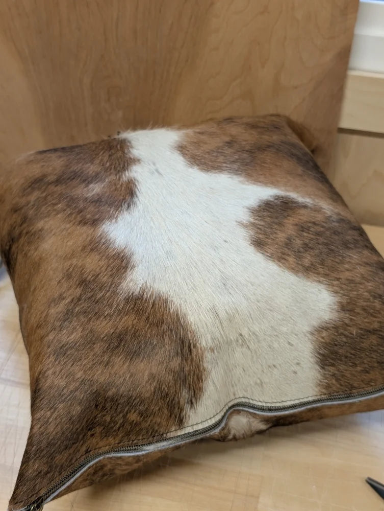 Brown and white cowhide mini moo cushion with visible zipper edge by angus oliver canada for cozy decor