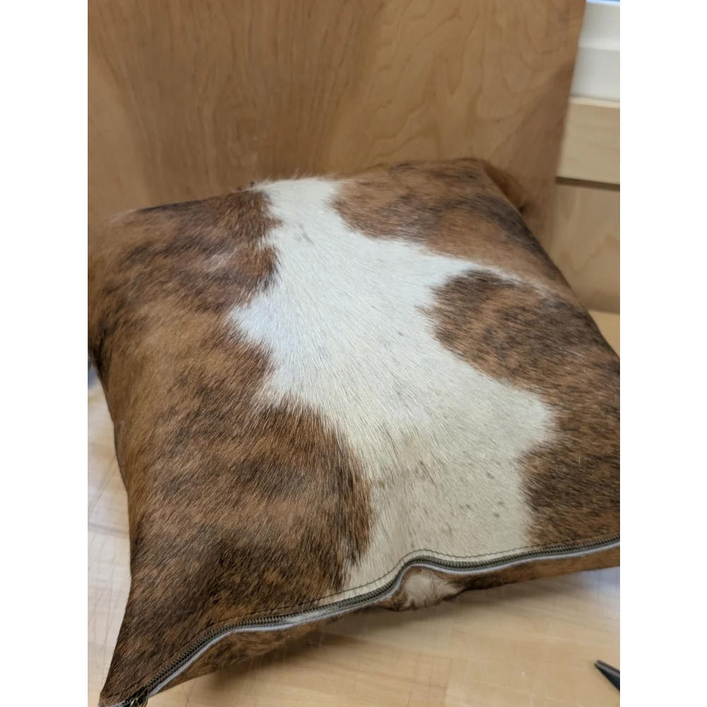 Brown and white cowhide mini moo cushion with visible zipper edge by angus oliver canada for cozy decor