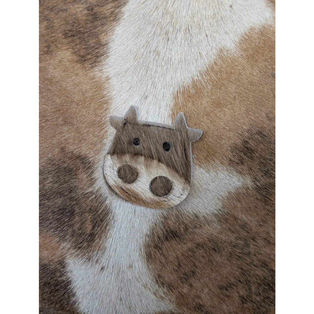 A charming mini moo brooch shaped like a brown and white cow made from textured leather by angus oliver canada