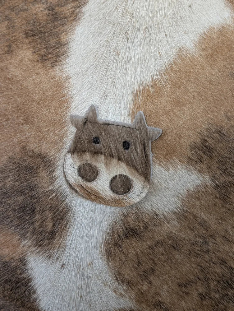 A charming mini moo brooch shaped like a brown and white cow made from textured leather by angus oliver canada