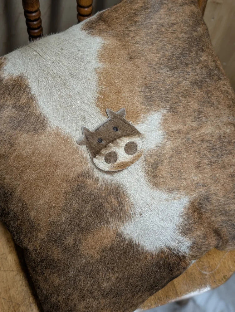 A mini moo angus oliver double sided cowhide cushion with brown white cow pattern and cute stitched cow face from canada