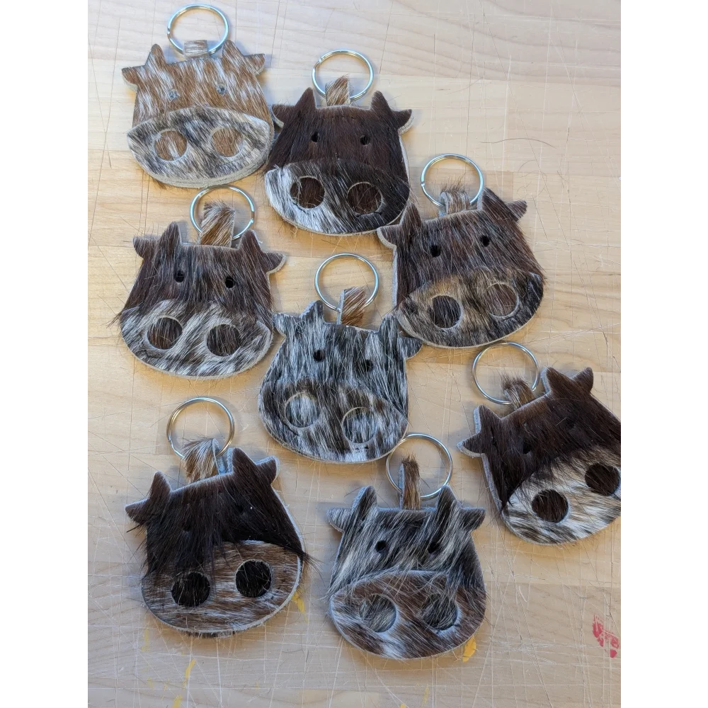 Mini moo cow-shaped keychain made of brown and white cowhide with black stitched eyes and metal ring by angus oliver canada