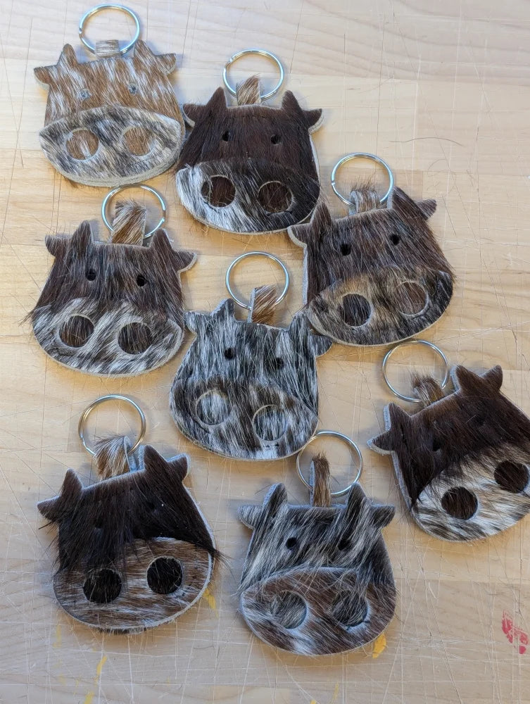 Mini moo cow-shaped keychain made of brown and white cowhide with black stitched eyes and metal ring by angus oliver canada
