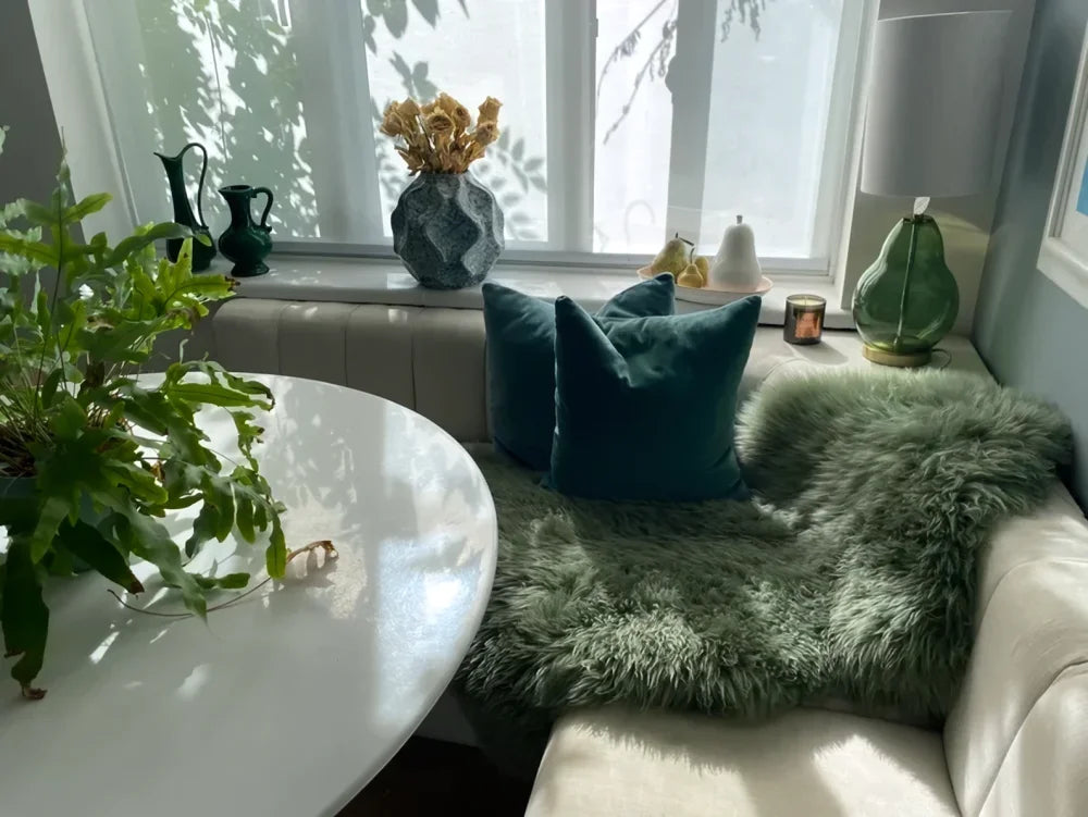 A matte gray ceramic vase with geometric pattern holds dried flowers next to a minty green merino sheepskin arriving mid october