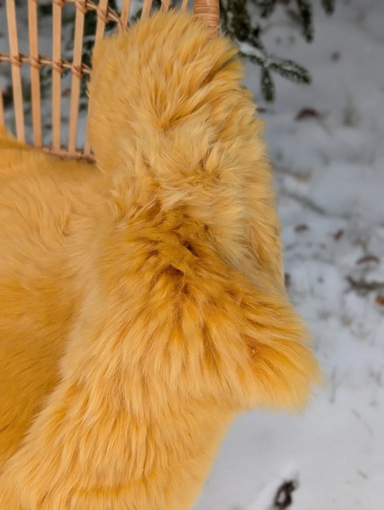 A plush mustard yellow merino sheepskin faux fur throw draped over a wicker chair for cozy seating