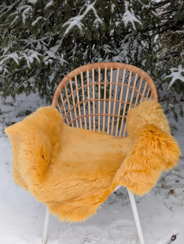 A vibrant mustard yellow merino sheepskin throw draped over a rattan chair with white metal legs outdoors