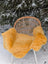 A vibrant mustard yellow merino sheepskin throw draped over a rattan chair with white metal legs outdoors