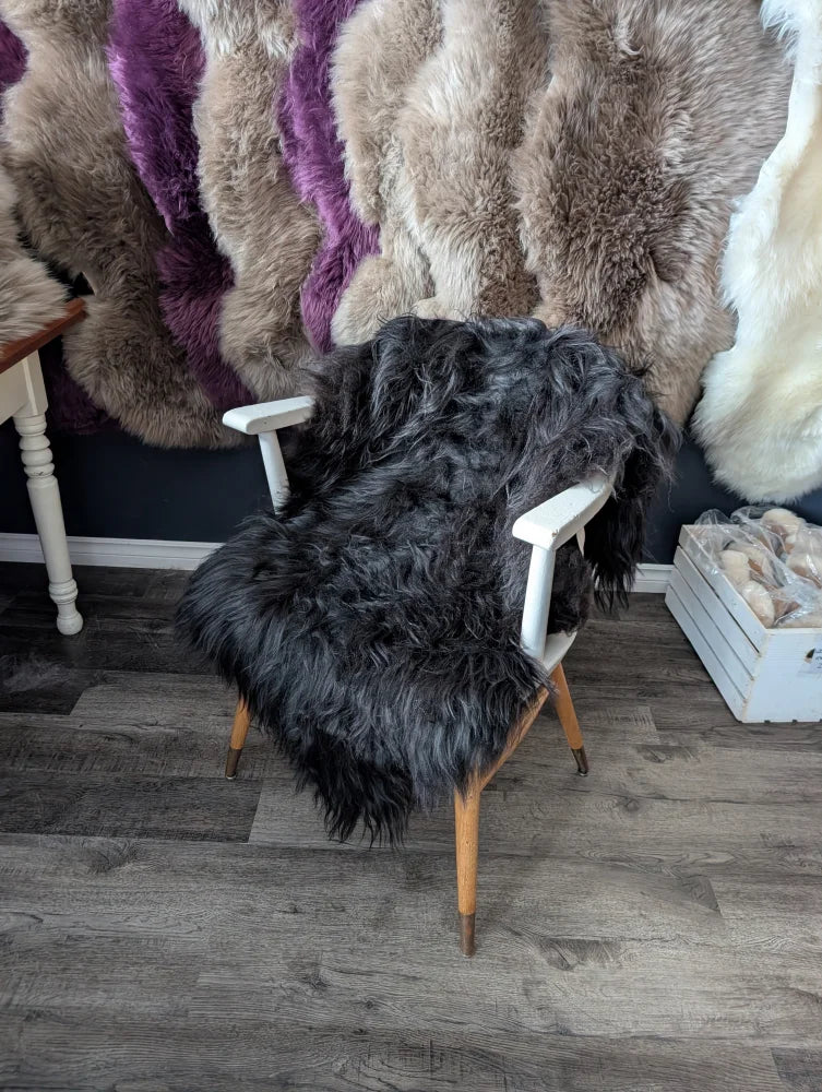 Black shaggy natural long wool icelandic sheepskins draped over white wooden chair with tapered legs