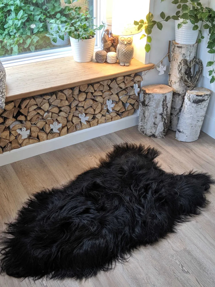 Black fluffy natural blacky long wool icelandic sheepskin rug with dense fur on light wood floor