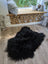 Black fluffy sheepskin rug with long wool icelandic fibers and natural irregular shape perfect for cozy decor