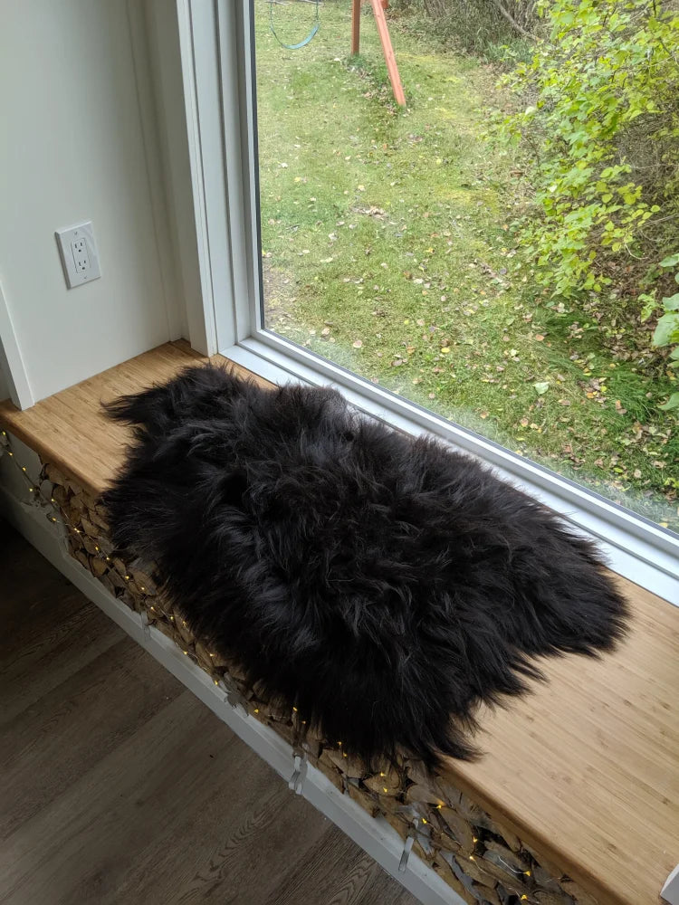 Black fluffy natural blacky long wool icelandic sheepskin rug resting on wooden windowsill with wool icelandic texture