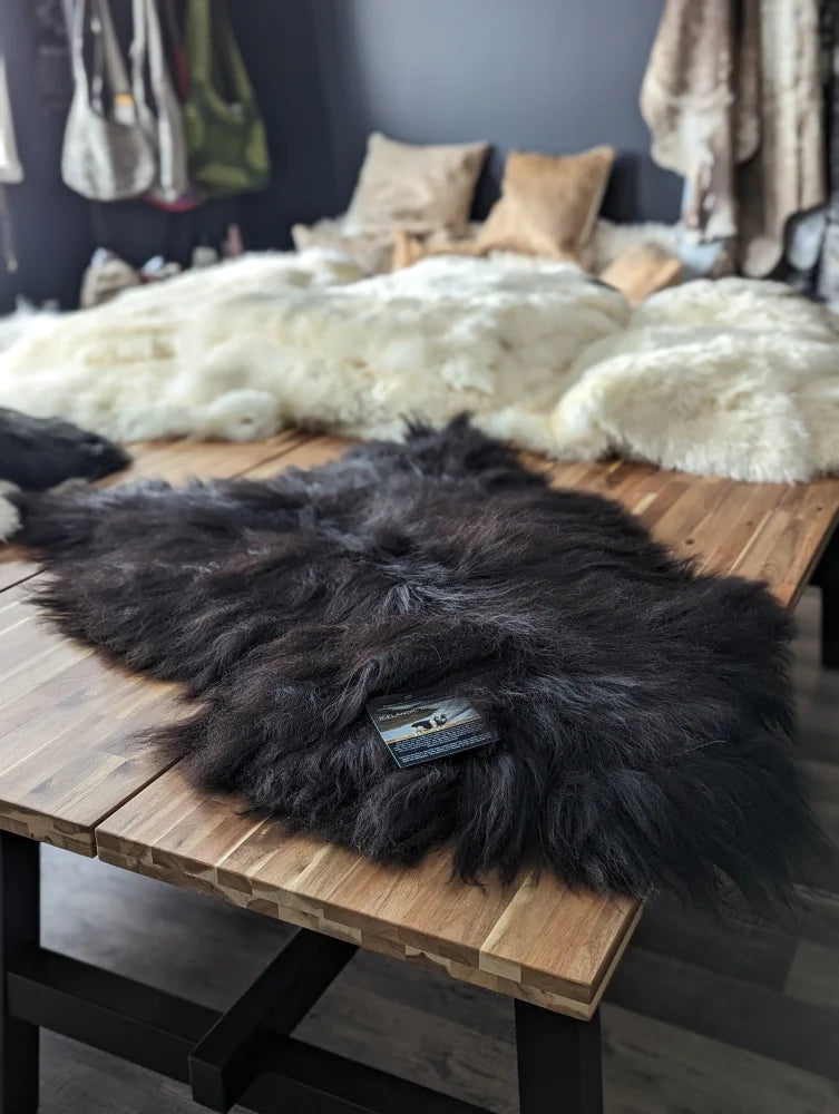 Dark thick-furred natural blacky long wool icelandic sheepskin rug resting on wooden table perfect for cozy decor