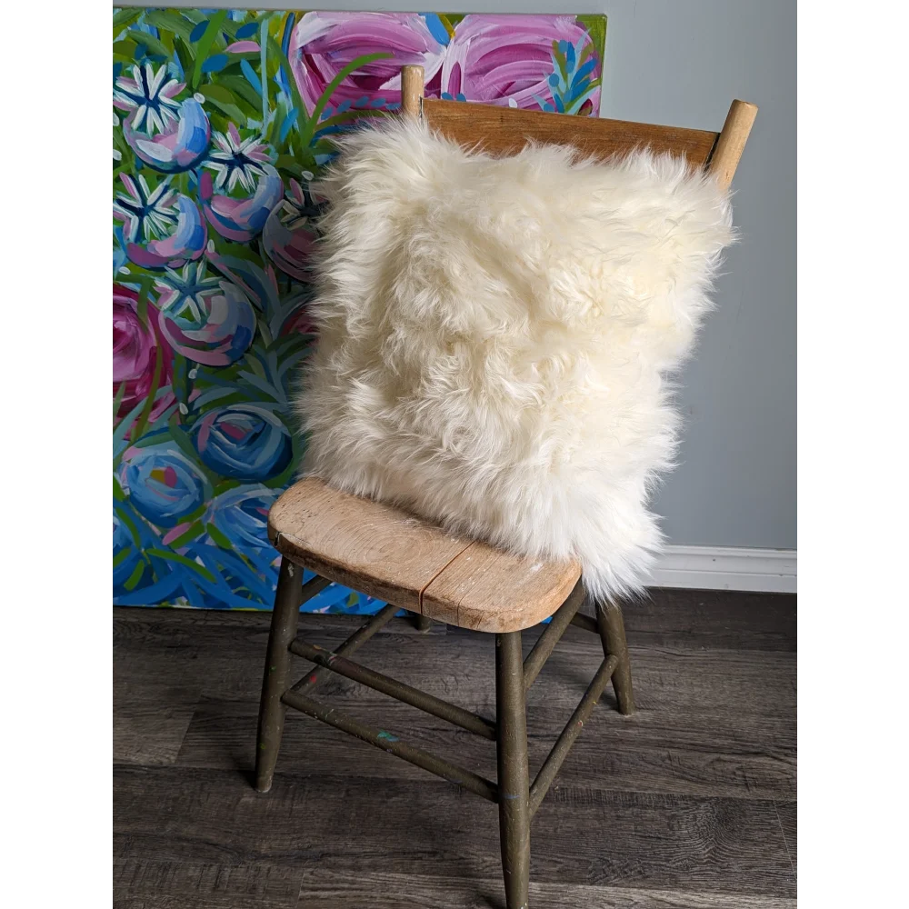 Cozy white sheepskin cushion on wooden chair with floral art background