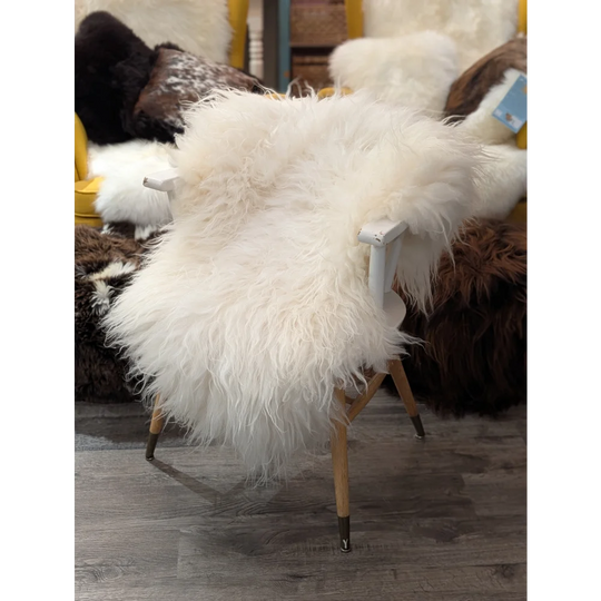 A plush white icelandic sheepskin rug draped over a modern chair with light wood legs and dark metal feet