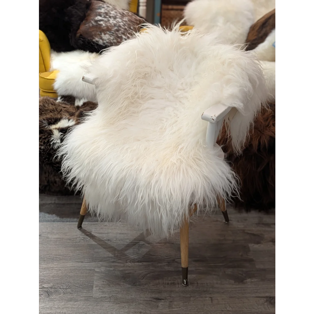A natural white icelandic sheepskin rug draped over a chair with light wood legs and dark metal feet