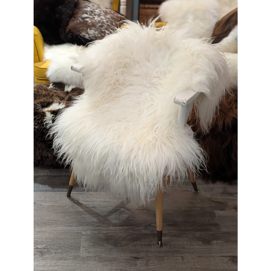 A natural white icelandic sheepskin rug draped over a chair with light wood legs and dark metal feet