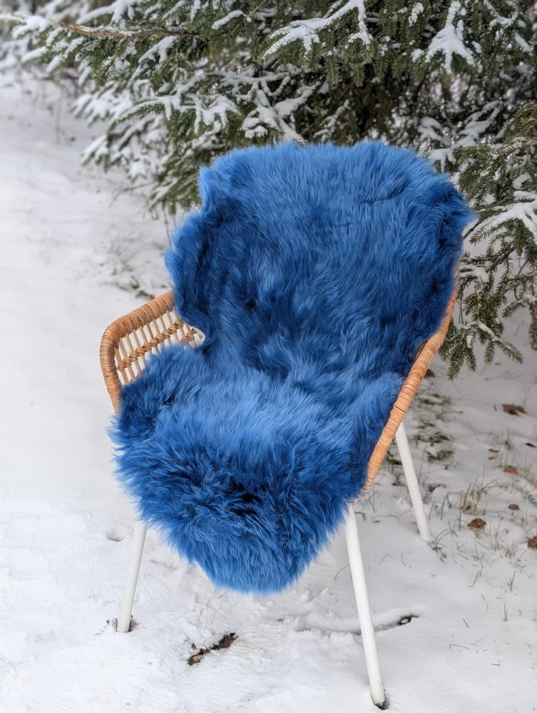 Vibrant navy blue merino sheepskin throw draped over wicker chair in snowy mid october landscape