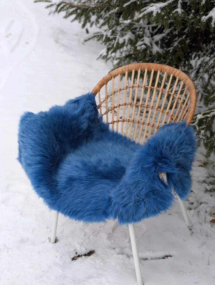 A vibrant blue merino sheepskin fluffy chair cover draped over a woven wicker chair perfect for mid october cozy vibes