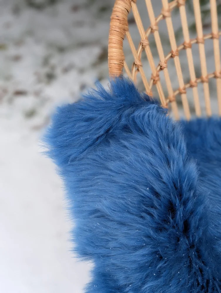 A vibrant blue merino sheepskin faux fur throw draped over a wicker chair perfect for mid october cozy vibes