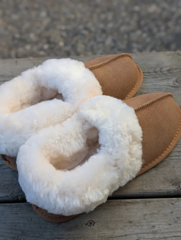 Tan suede moccasin slippers with plush white shearling lining offering ultimate sheepskin comfort at home