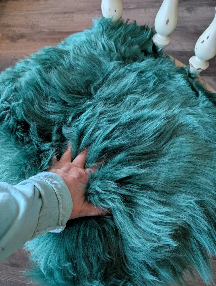 Gorgeous green merino sheepskin chair pad with teal faux fur throw and white wooden legs