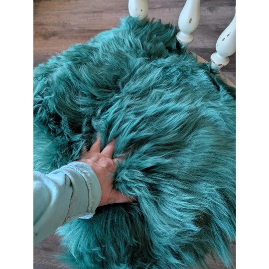 Gorgeous green merino sheepskin chair pad with teal faux fur throw and white wooden legs