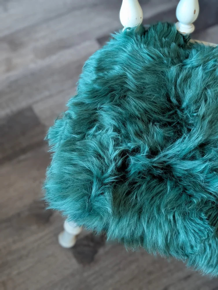 Teal faux fur purse with white wooden handles on gorgeous green merino sheepskin chair pad