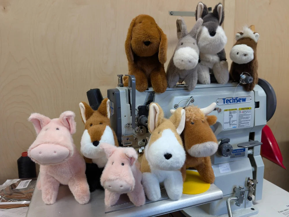 A gray industrial techsew sewing machine with plush pink piggies stuffed animals arranged around it