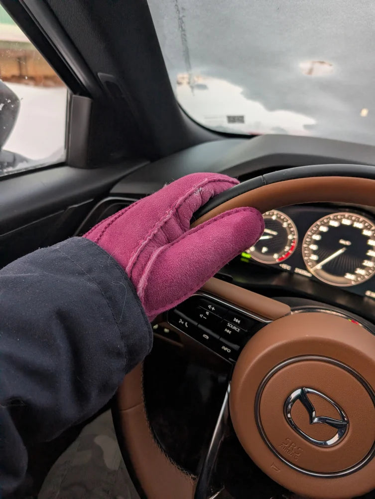 Hand wearing pink sheepskin gloves gripping Mazda steering wheel