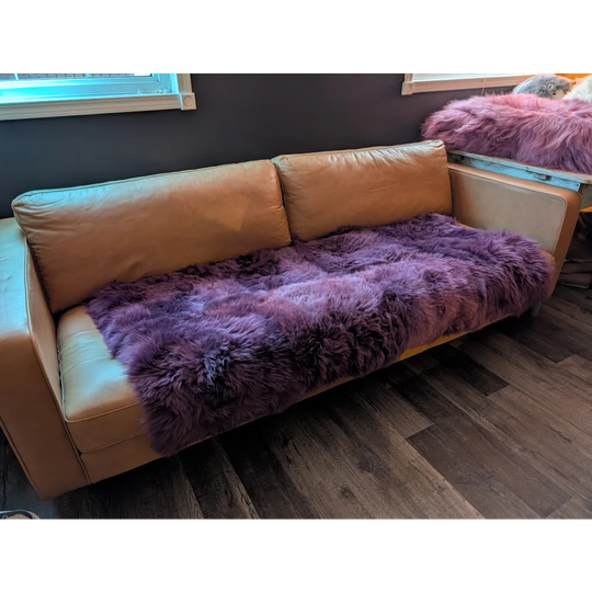 Tan leather couch with plush purple sheepskin area rug throw