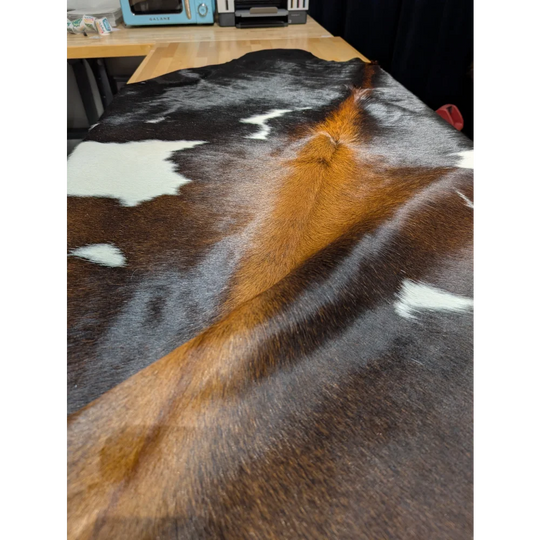 Extra large cowhide rug with brown, black, white patches on wood