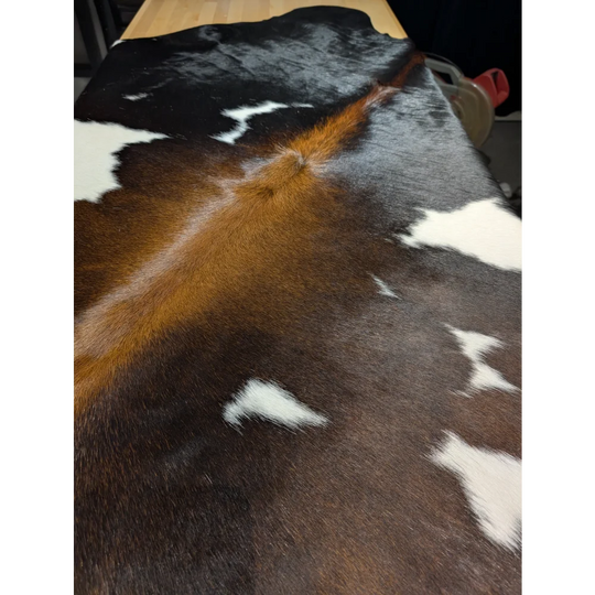 Extra large cowhide rug with brown, black, white patches on wood