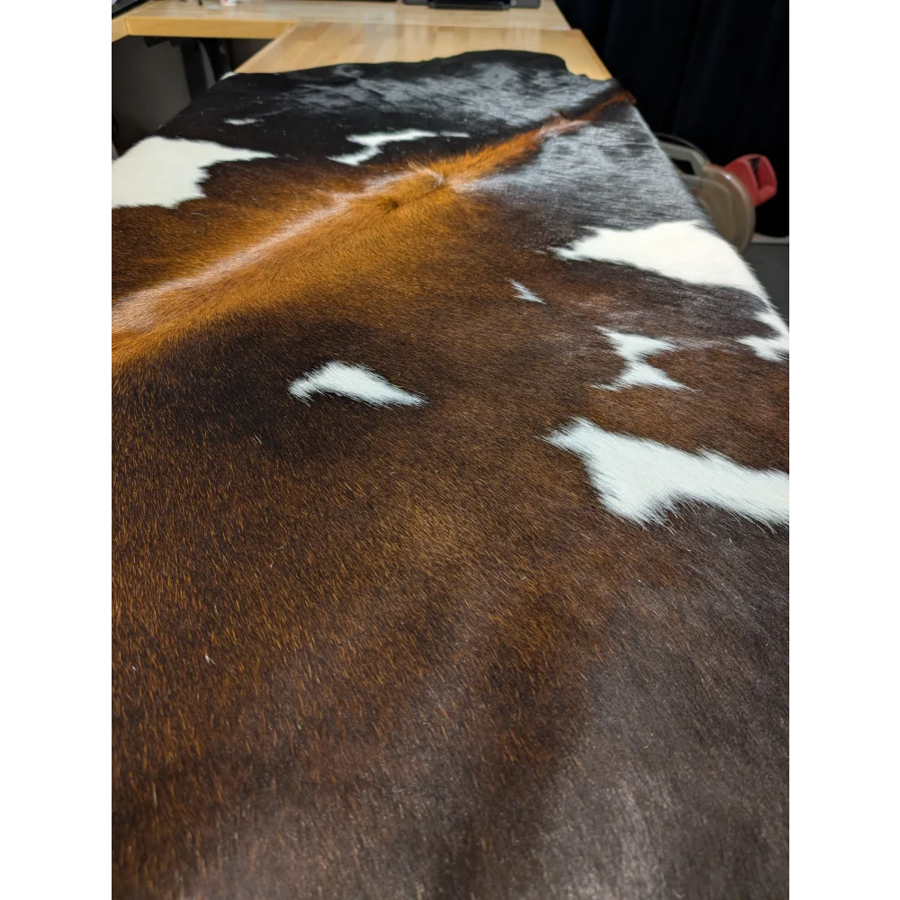 Extra large cowhide rug with brown, black, white patches on wood