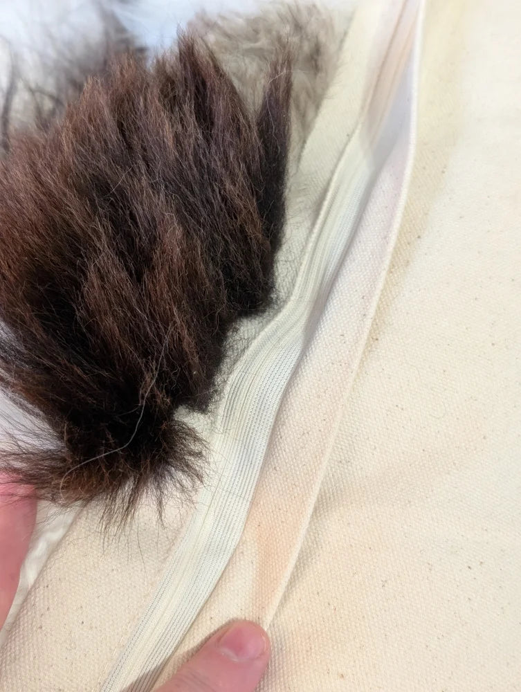 Back of ridiculously over the top sheepskin cushion with fluffy dark brown faux fur pom-pom on zipper seam