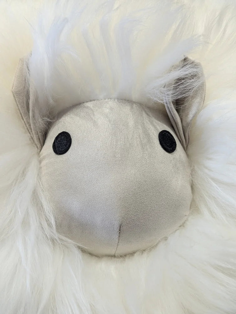 A plush white rotund sheep cushion with soft merino sheepskin fur and a satin silver face with black button eyes