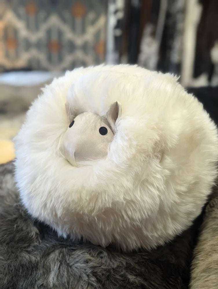 A plush round white rotund sheep cushion made of soft merino sheepskin with a cute alpaca face perfect for cozy decor