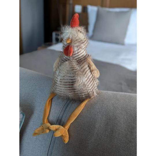 Rupert The Rooster plush chicken toy with striped pattern, orange beak on gray couch