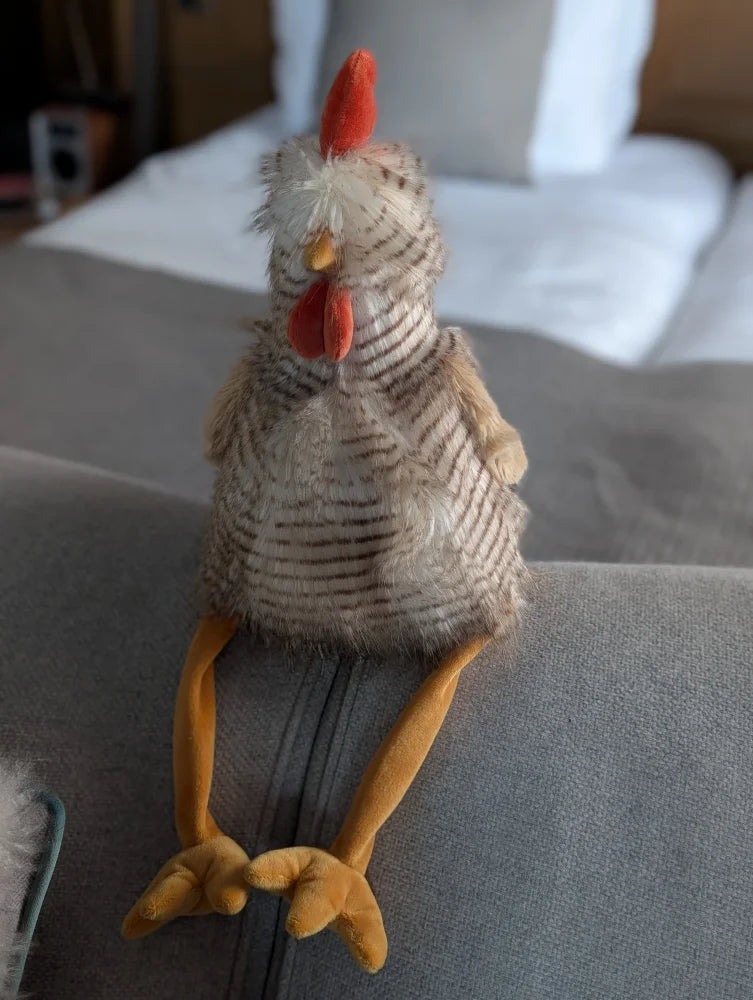 A plush chicken toy named rupert the rooster with striped gray and white body and orange feet from nana huchy